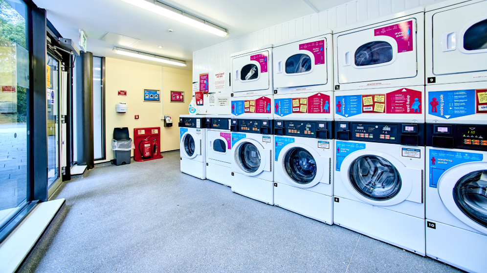 A row of 5 washing machines with dryers stacked on top